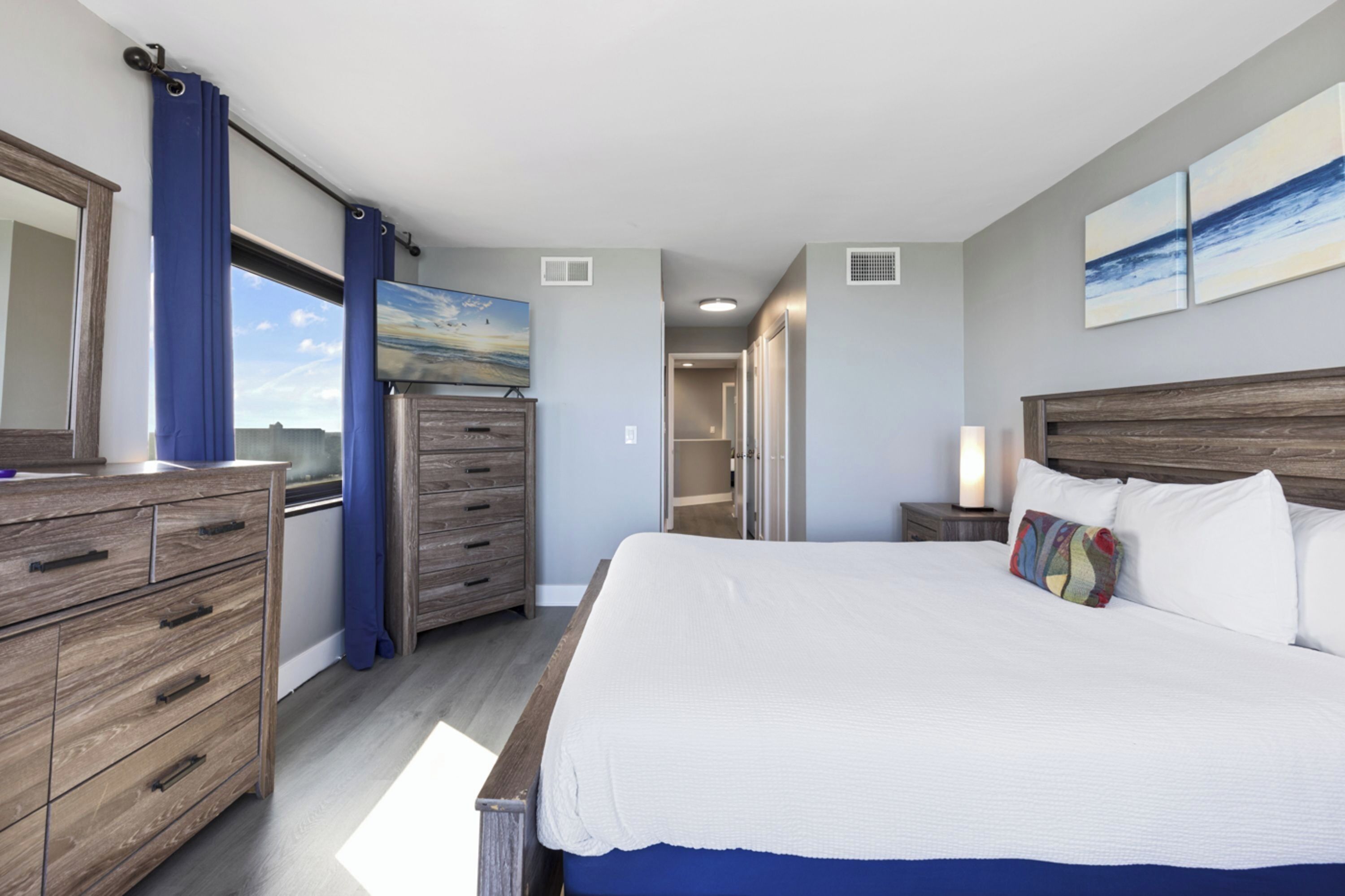 A bedroom with a large bed, wooden dresser, and a view of the outdoors through a window.
