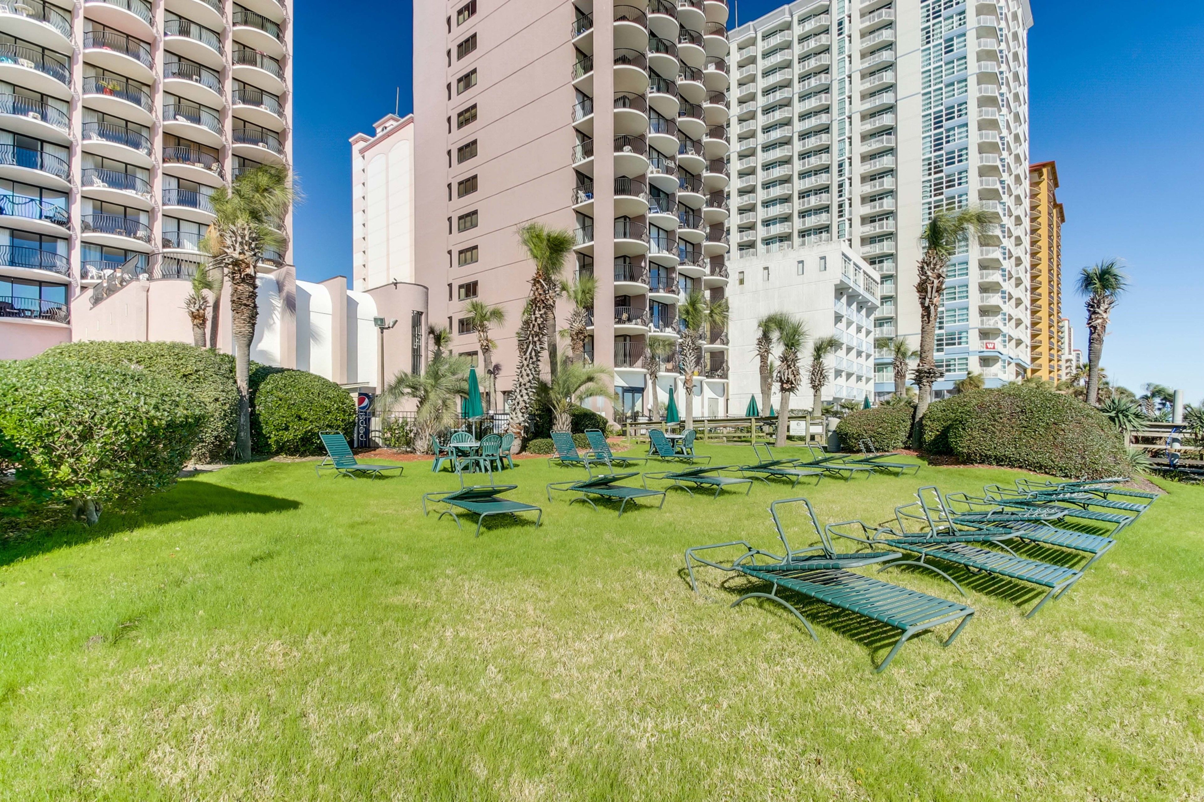 A hotel courtyard with green lawn, lounge chairs, and tall buildings in the background.