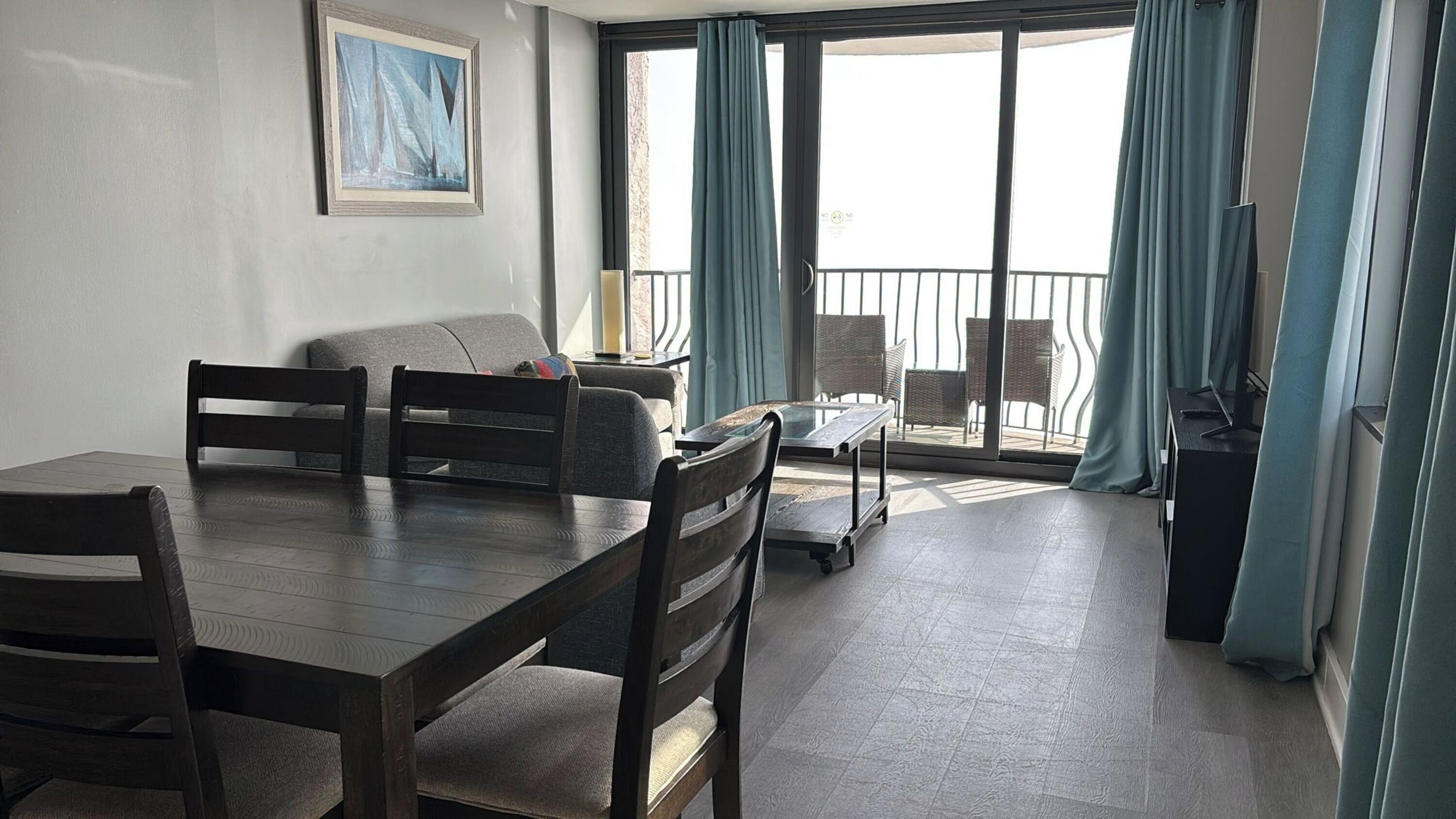 A dining area with a table and chairs, a sofa, and a balcony with wicker chairs and a table.