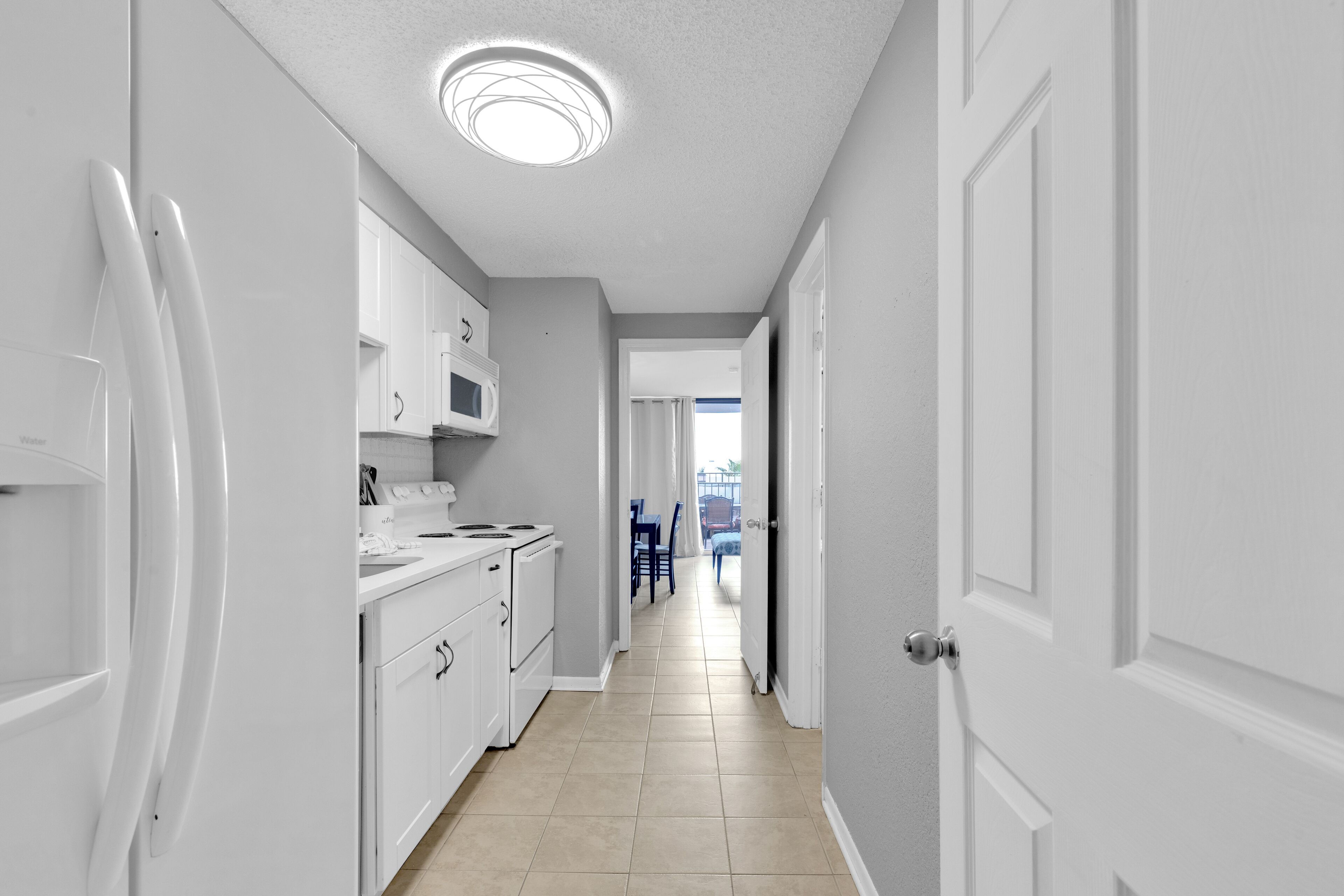 A narrow hallway with white cabinets, a microwave, and a refrigerator.