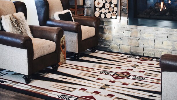 Un salon chaleureux avec une cheminée en pierre, des fauteuils en cuir et un tapis à motifs.