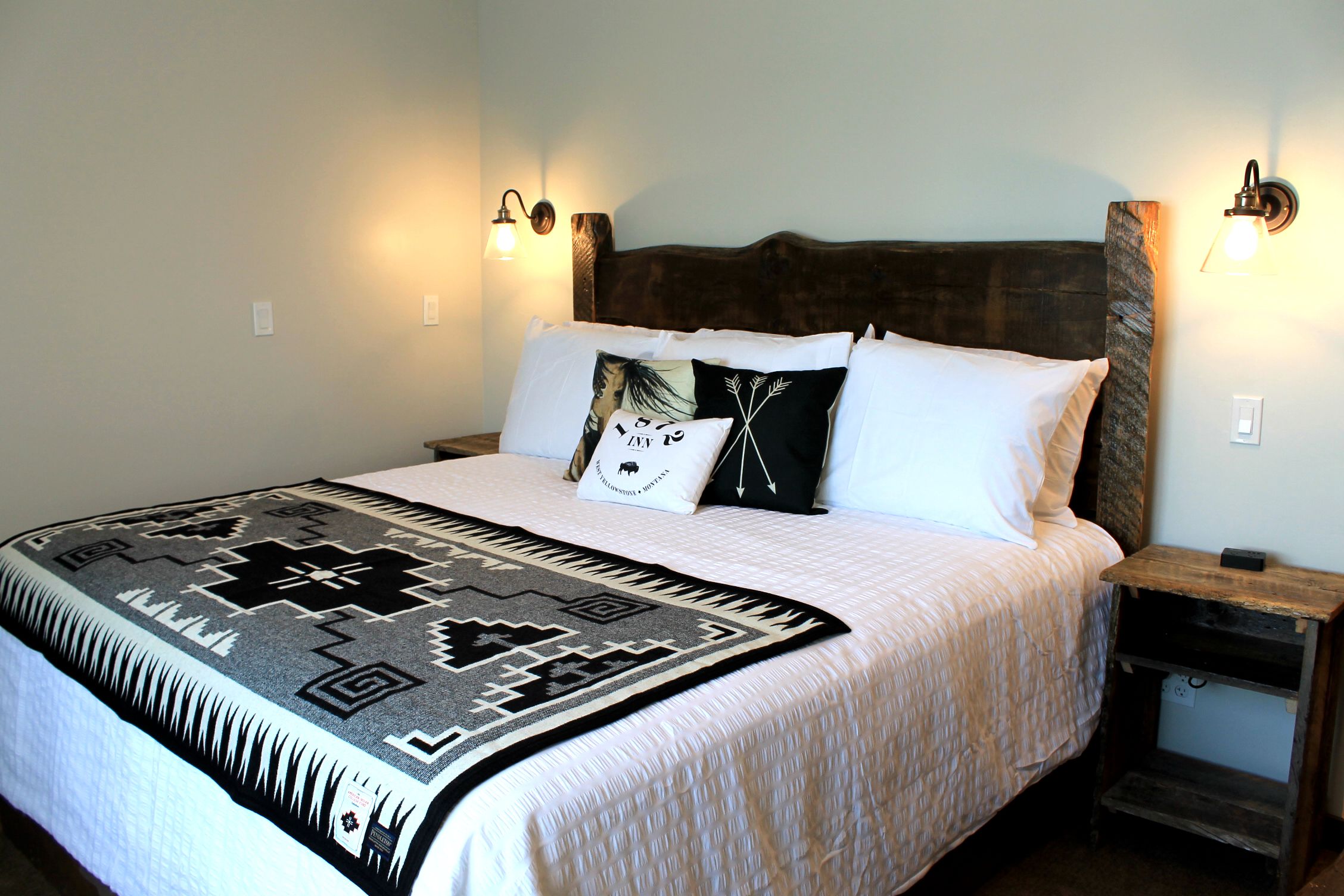 A bed with a patterned blanket, two pillows, and a wooden headboard. There are two bedside tables with lamps.