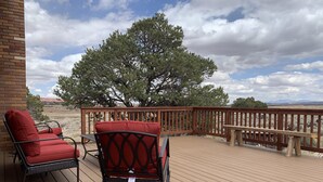 A wooden deck with two red cushioned chairs and a bench, overlooking a landscape with trees and distant mountains. - Rustic isolation near Capitol Reef National Park (Teasdale)