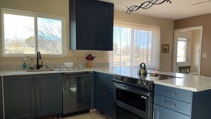 A modern kitchen with dark blue cabinets, a stainless steel dishwasher, a double oven, and a large window providing natural light. - Rustic isolation near Capitol Reef National Park (Teasdale)