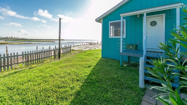Una casa turchese con porta bianca, un piccolo portico e vista sulla spiaggia e sul mare.