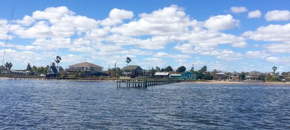 A waterfront property with a pier extending into the water, surrounded by residential buildings and palm trees.