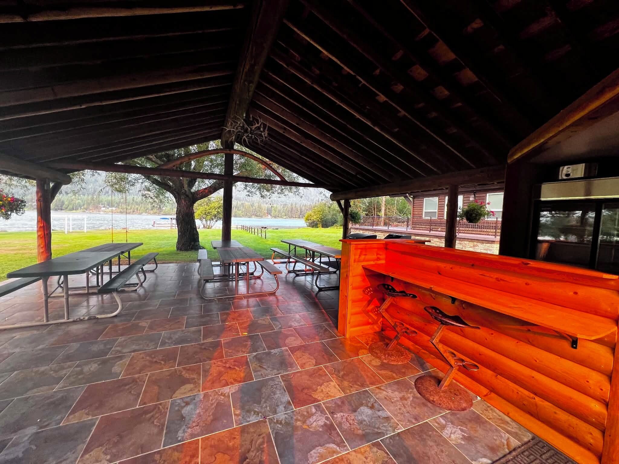An outdoor covered patio with picnic tables, a barbecue grill, and a wooden bench.
