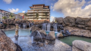 A hotel with a pool area featuring rock formations, waterfalls, and a rope swing.
