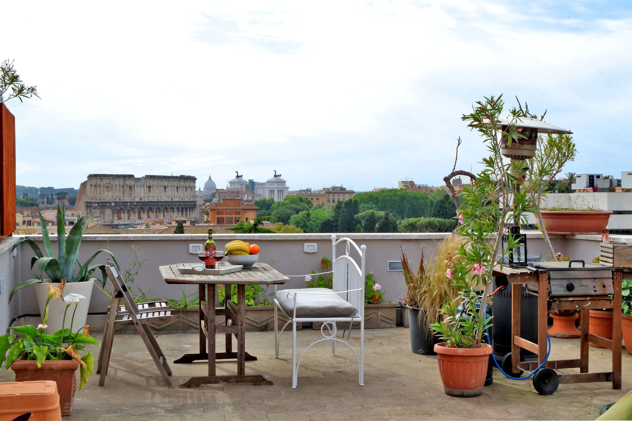 A rooftop terrace with a table, chair, potted plants, and a grill.