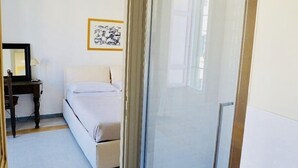 A hotel room with a shower, a bed, a desk, and a framed picture on the wall. - Rome Apartment Rentals Colosseum View - Roof Terrace with 2BR/2BATH Wi-Fi (Roma)