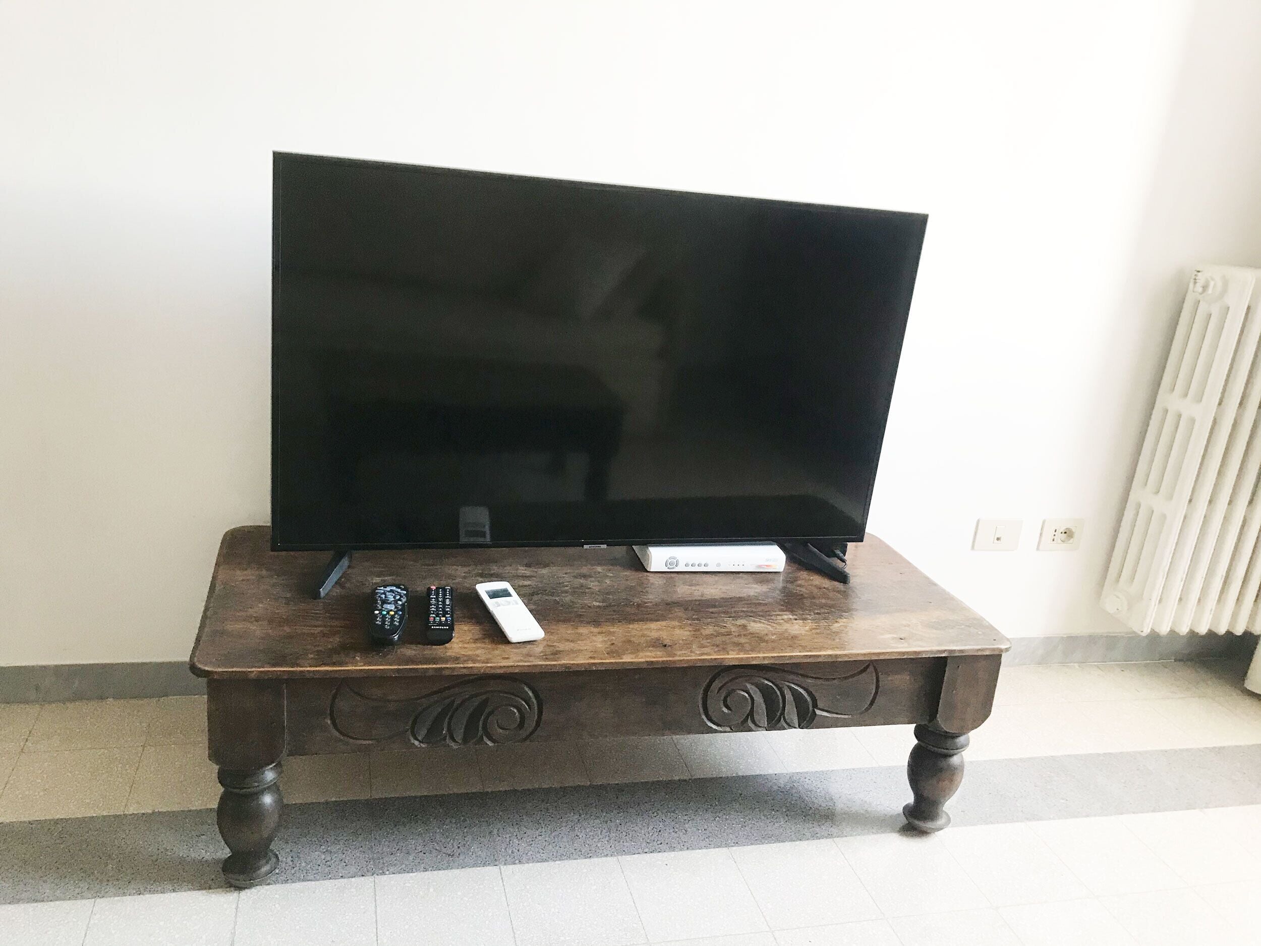 A television on a wooden table with remote controls and a white device.