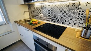 A kitchen with a black induction cooktop, a sink with a faucet, and a backsplash with geometric tile patterns. - Rome Apartment Rentals Colosseum View - Roof Terrace with 2BR/2BATH Wi-Fi (Roma)