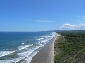 Un paysage côtier avec une plage de sable, des vagues de l’océan et des collines à l’horizon.