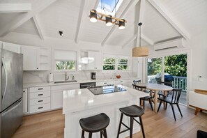 A modern kitchen with white cabinetry, a large island, and a dining area with a table and chairs. - Cycle or Walk to Hanalei Bay (Hanalei)