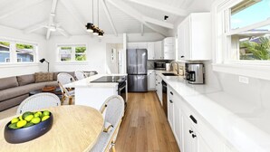 Cocina moderna con armarios blancos, una isla central y un comedor con mesa y sillas redondas.