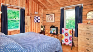 A wooden cabin room with two beds, a television, a dresser, and a window with curtains.