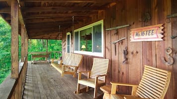 Une véranda en bois avec des chaises et un banc en bois, une pancarte indiquant « Trou n° 16 », et une vue sur la verdure environnante.