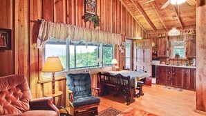 A cozy cabin interior with a dining area, a large window, and a kitchen.