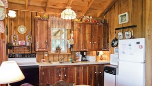 A rustic kitchen with wooden cabinets, a stove, a refrigerator, and a dining area with a table and chairs.