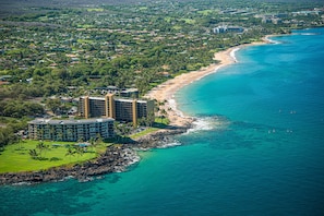 An aerial view of a coastal resort area with a beachfront, a large hotel complex, and surrounding greenery.