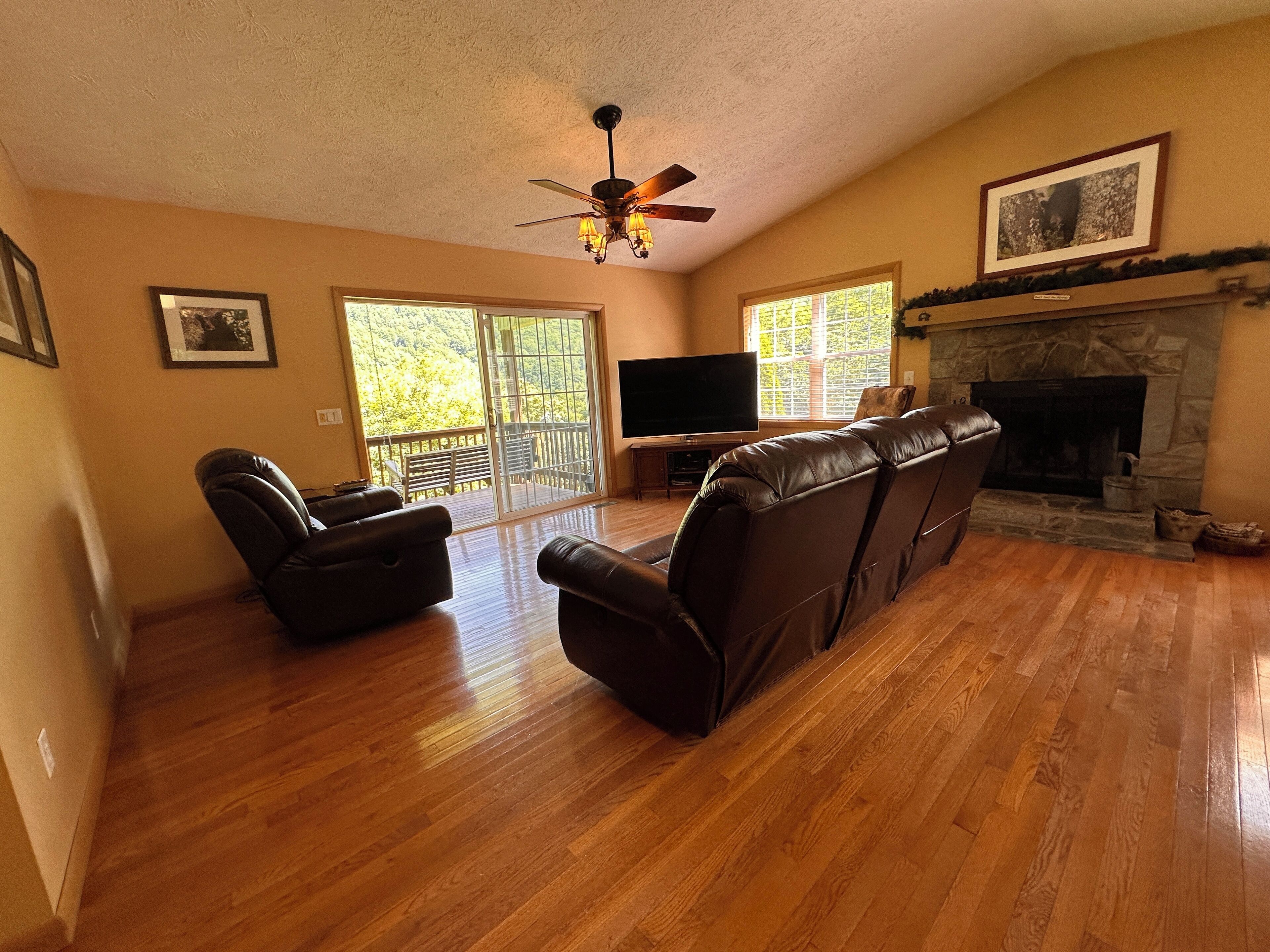 A spacious living room with a fireplace, leather sofas, a flat-screen TV, and a balcony with sliding doors.