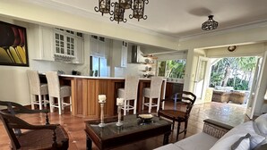 Un grand espace de vie comprenant un canapé, des fauteuils, une table basse et une cuisine en arrière-plan.