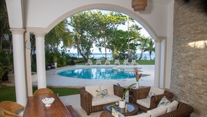 Un espace extérieur abrité, aménagé avec des meubles en osier, une piscine et une vue sur l’océan.