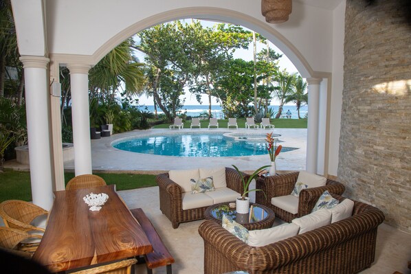 A covered outdoor area with wicker furniture, a pool, and a view of the ocean. - On The Beach Luxury Mediterranean Villa . Gated Community Partial or full staff (Cabarete)