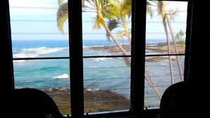 A room with a large window overlooking the ocean and palm trees. - Must see! Spectacular Direct Oceanfront Corner Unit  (Kailua-Kona)