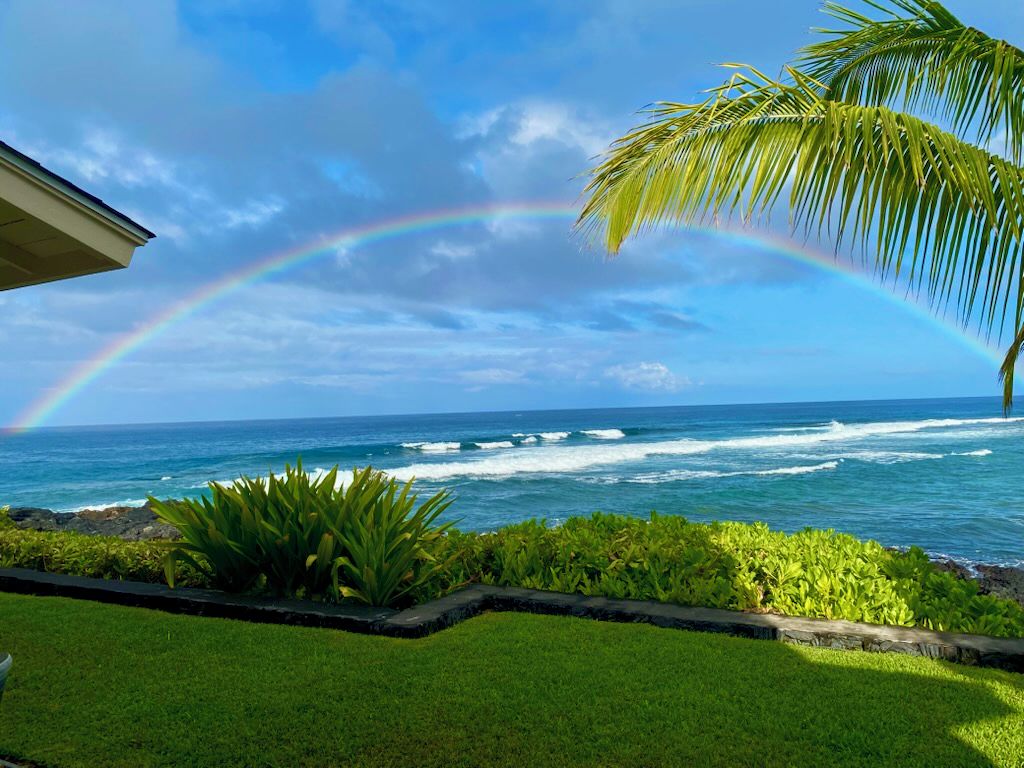 Une vue sur la côte, avec un ciel dégagé, des vagues sur l’océan et un arc-en-ciel.