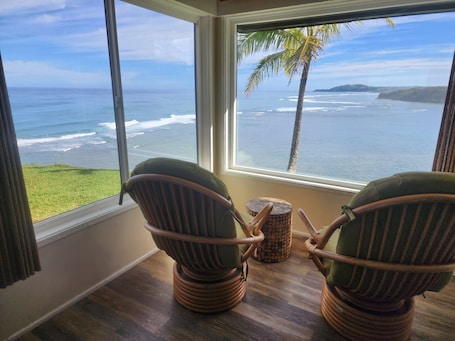 A room with two wicker chairs facing a large window overlooking the ocean.