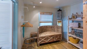 A small, rustic room with a wooden bed, a window with blinds, a shelf with towels, and a hanging light fixture.