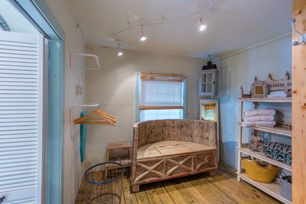 Una habitación pequeña y rústica con una cama de madera, una ventana con persianas, un estante con toallas y una lámpara colgante.