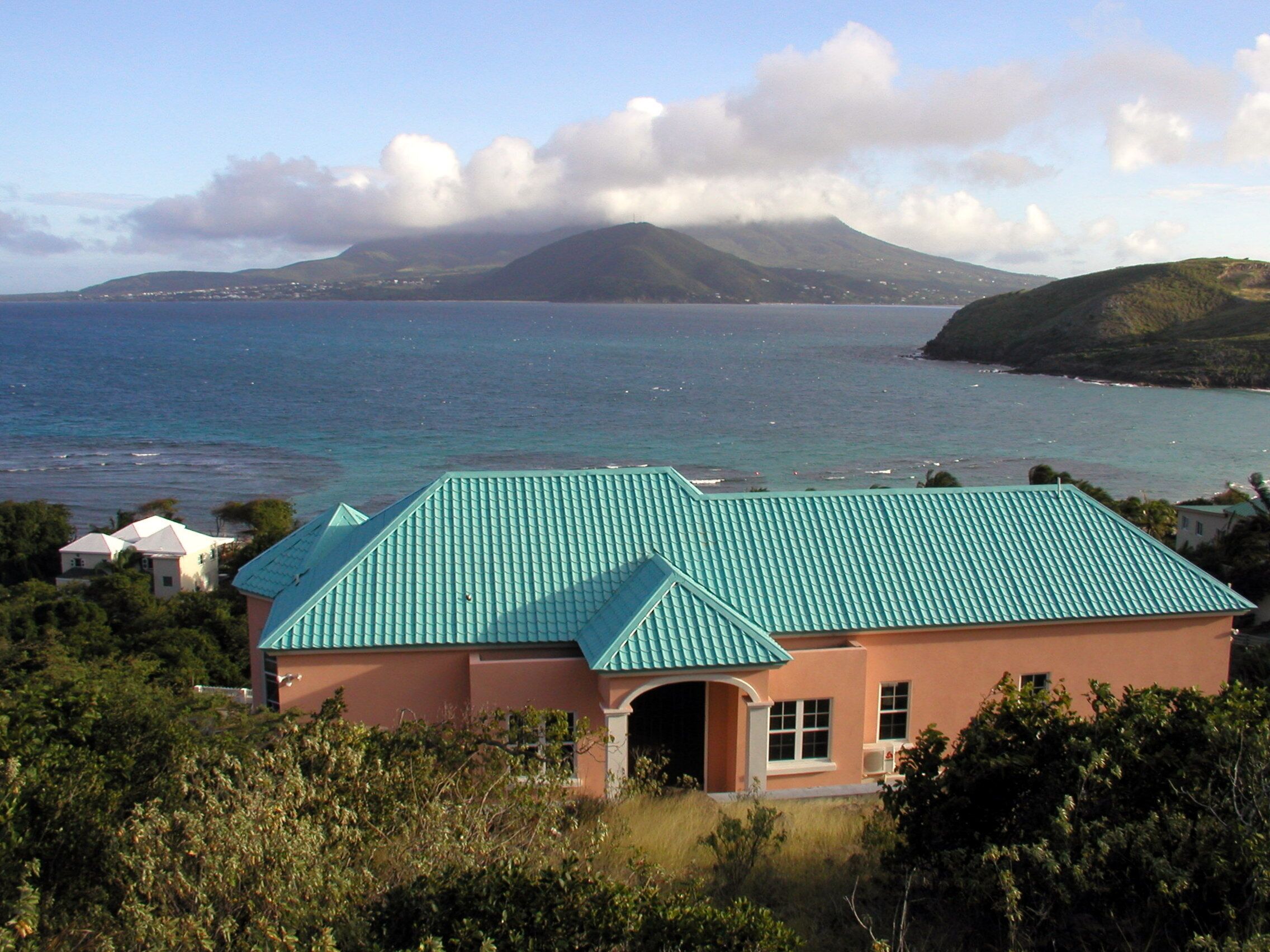 Une maison dotée d’un toit végétalisé, entourée d’une végétation luxuriante et offrant une vue sur une mer calme, avec une montagne en toile de fond.
