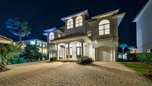 A large, two-story house with a spacious driveway and a well-lit entrance. - Over the Top | 7 Bedroom! | Clubhouse Amenities! Pickleball, Gym & Hot Tub! | Pet-Friendly Escape in Destin | Private Pool | Gulf Views! Wedding Friendly! (Destin)