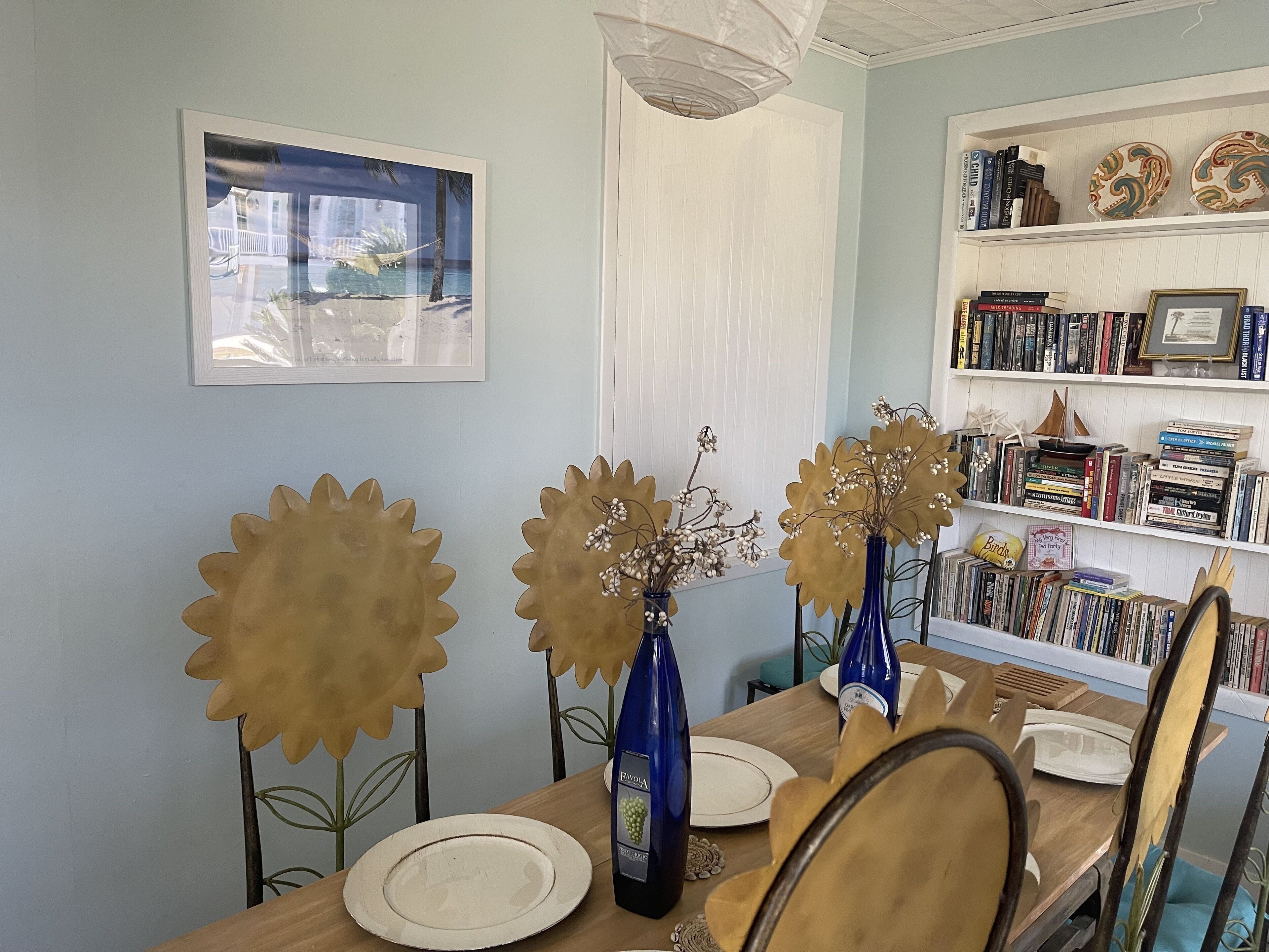 A dining area with a wooden table, blue vases with flowers, and a bookshelf filled with books and decorative items.