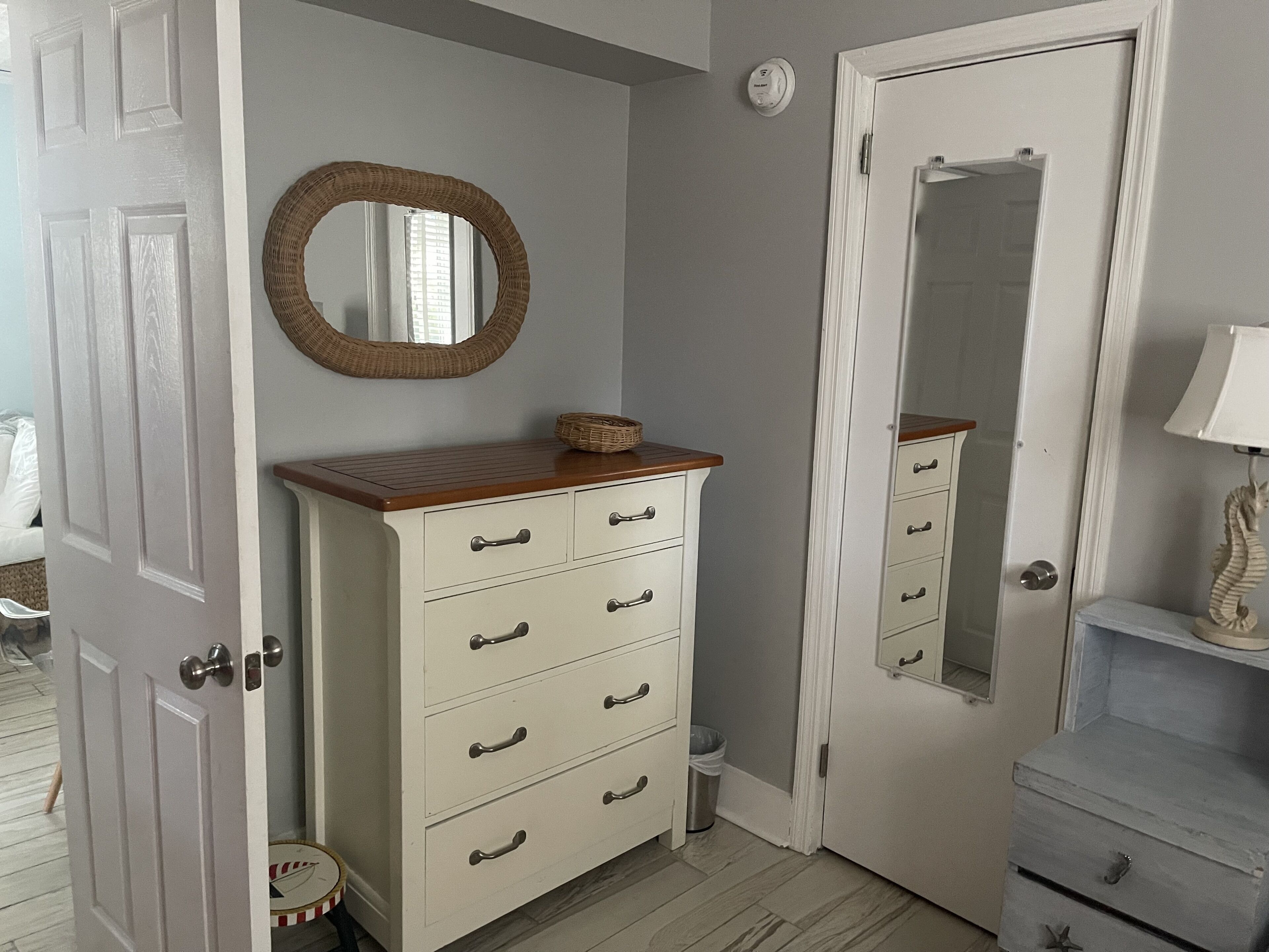 A room with a white dresser, a mirror, a small round table, and a door.