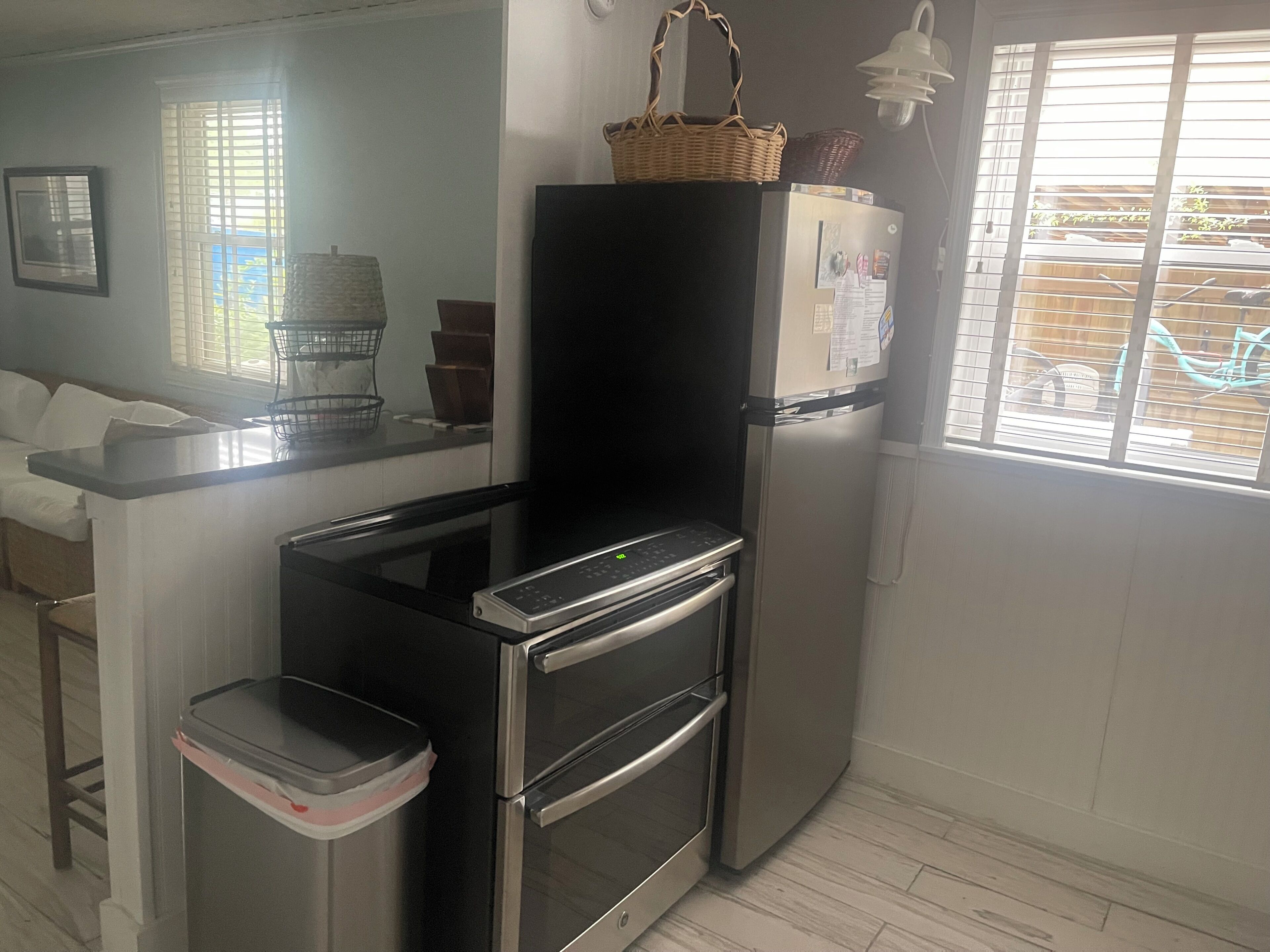 A compact kitchen with a refrigerator, oven, and a small trash bin.