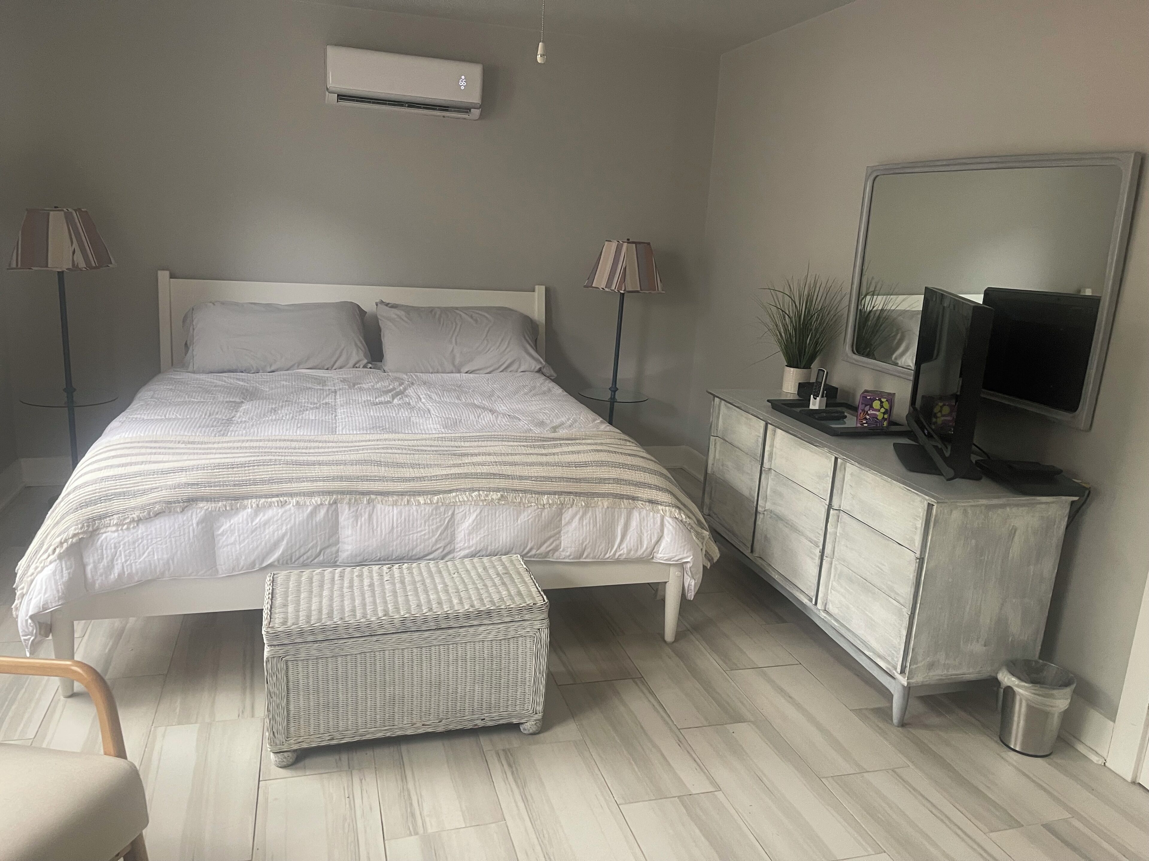 Quarto com cama, luminárias de cabeceira, cômoda, televisão e ar condicionado.