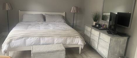 Quarto com cama, luminárias de cabeceira, cômoda, televisão e ar condicionado.