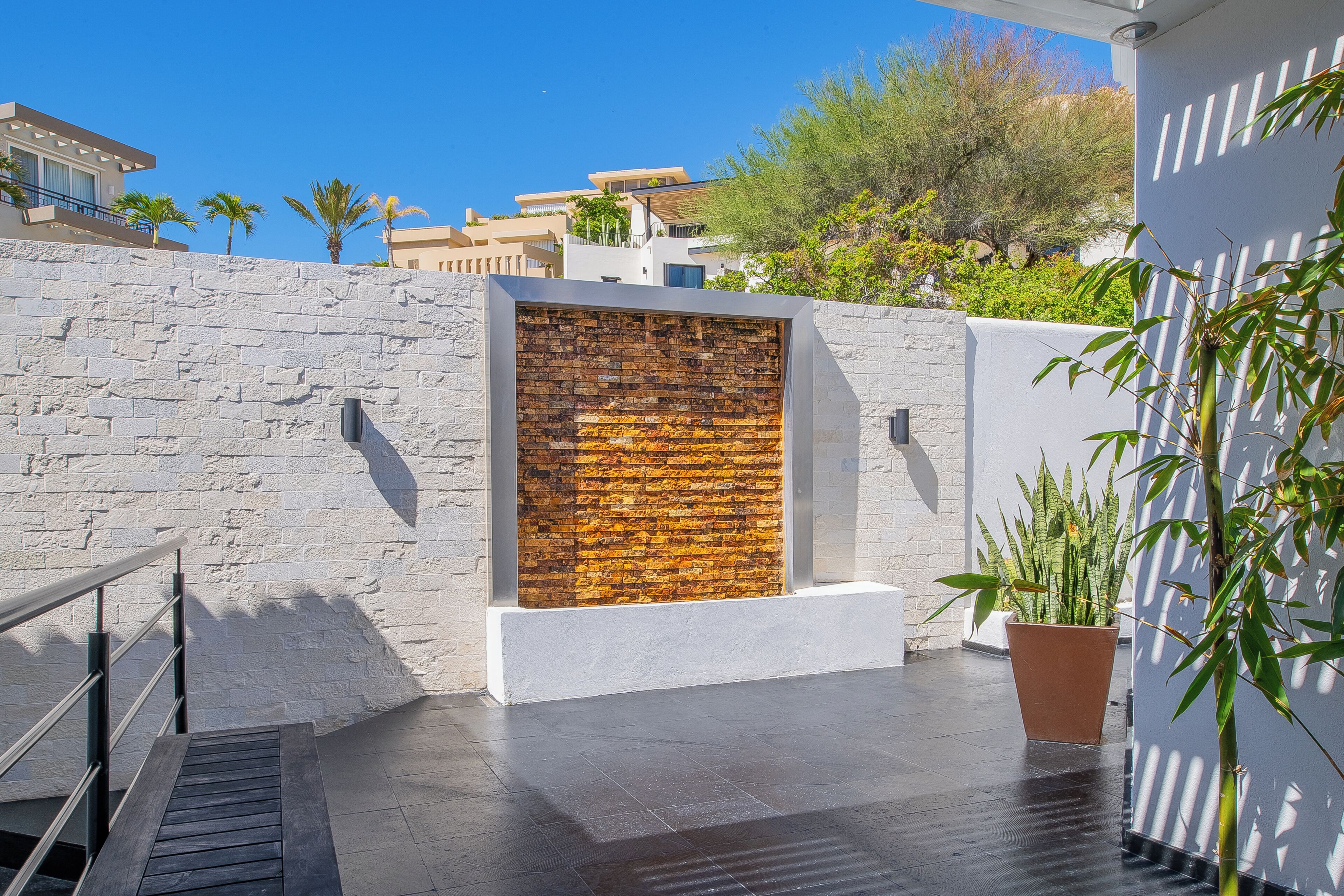 A modern outdoor area with a stone wall, a wooden bench, and a potted plant.