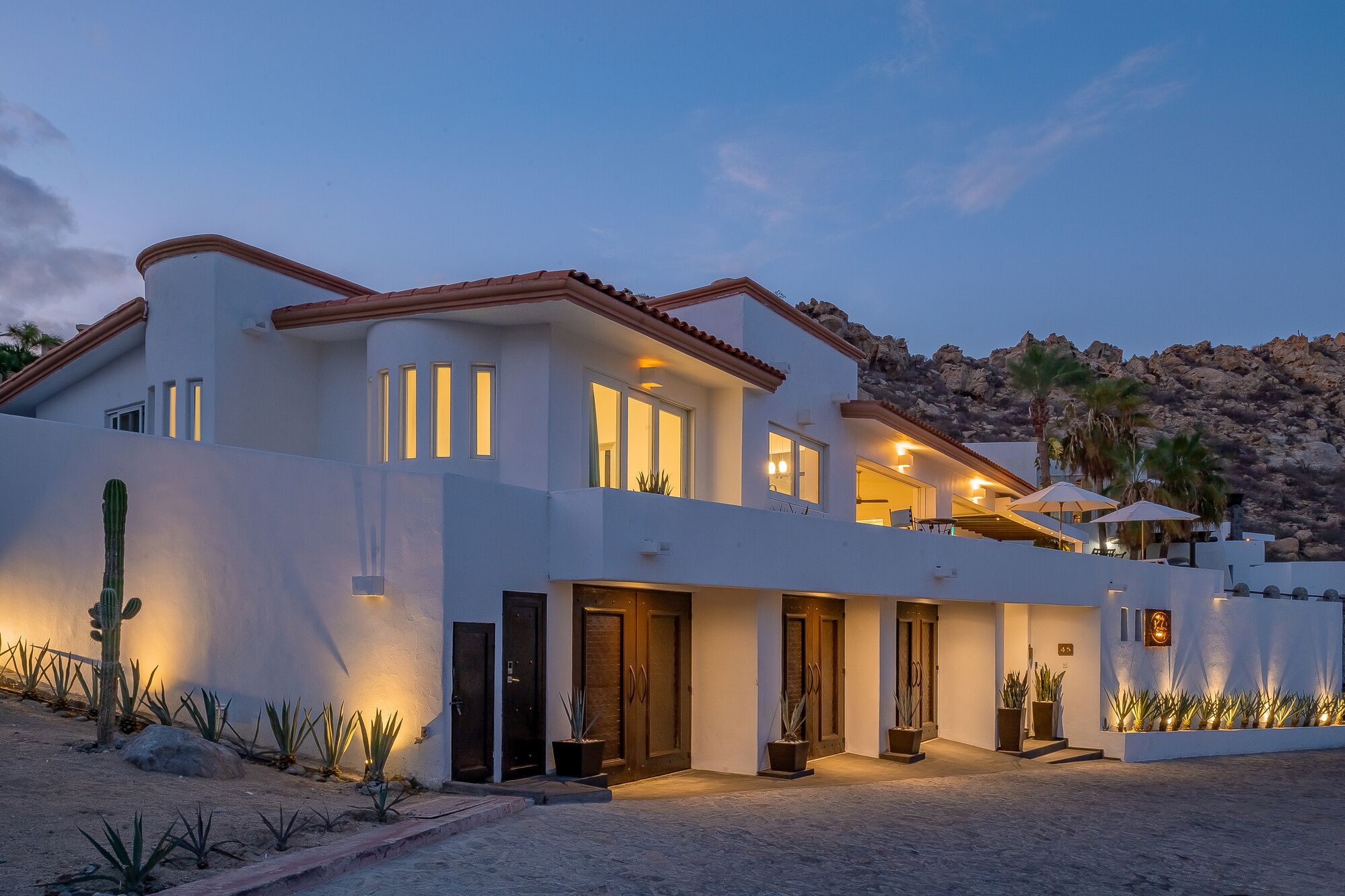 A modern two-story house with a desert garden, large windows, and a mountain backdrop.