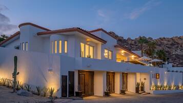 A modern two-story house with a desert garden, large windows, and a mountain backdrop.