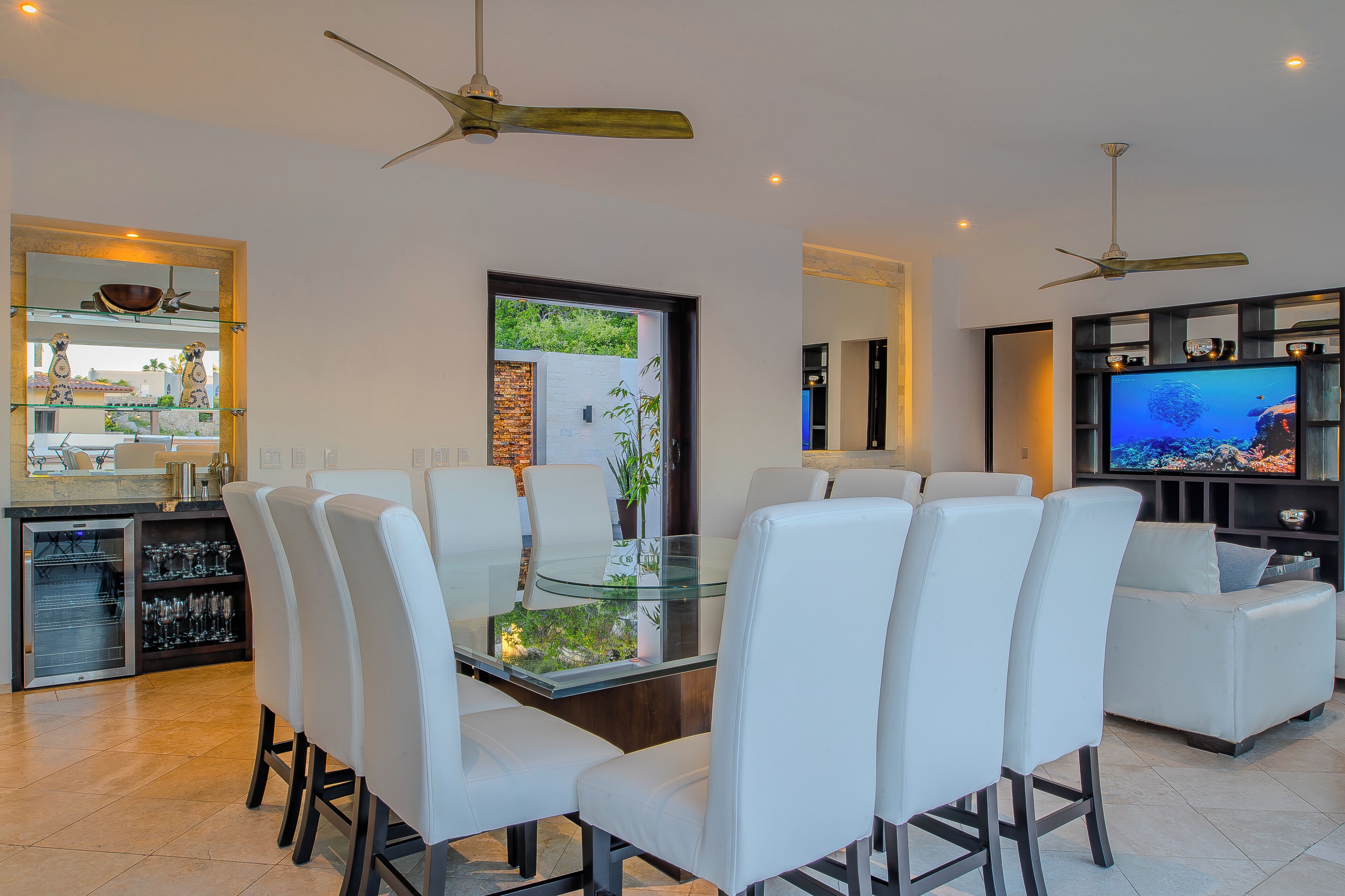 A modern living room with a glass-top dining table surrounded by white chairs, a sofa, and a television.