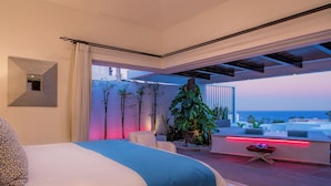 Un dormitorio moderno con una cama grande, vista al océano y un balcón con plantas y una luz roja.