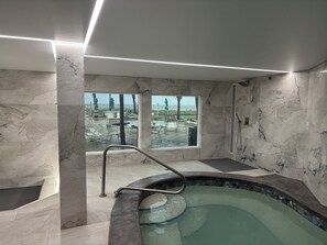 A spa area with a hot tub, marble walls, and a view of an outdoor pool area.
