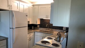 A modern kitchen with white cabinets, a granite countertop, a stainless steel refrigerator, a gas stove, and a black backsplash. - RIGHT ON THE BEACH! First Floor! Walk out slidingdoor  your steps from the beach (Panama City Beach)