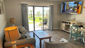 A living room with a sofa, a coffee table, a lamp, a television, and a view of the outdoors through a sliding glass door. - RIGHT ON THE BEACH! First Floor! Walk out slidingdoor  your steps from the beach (Panama City Beach)