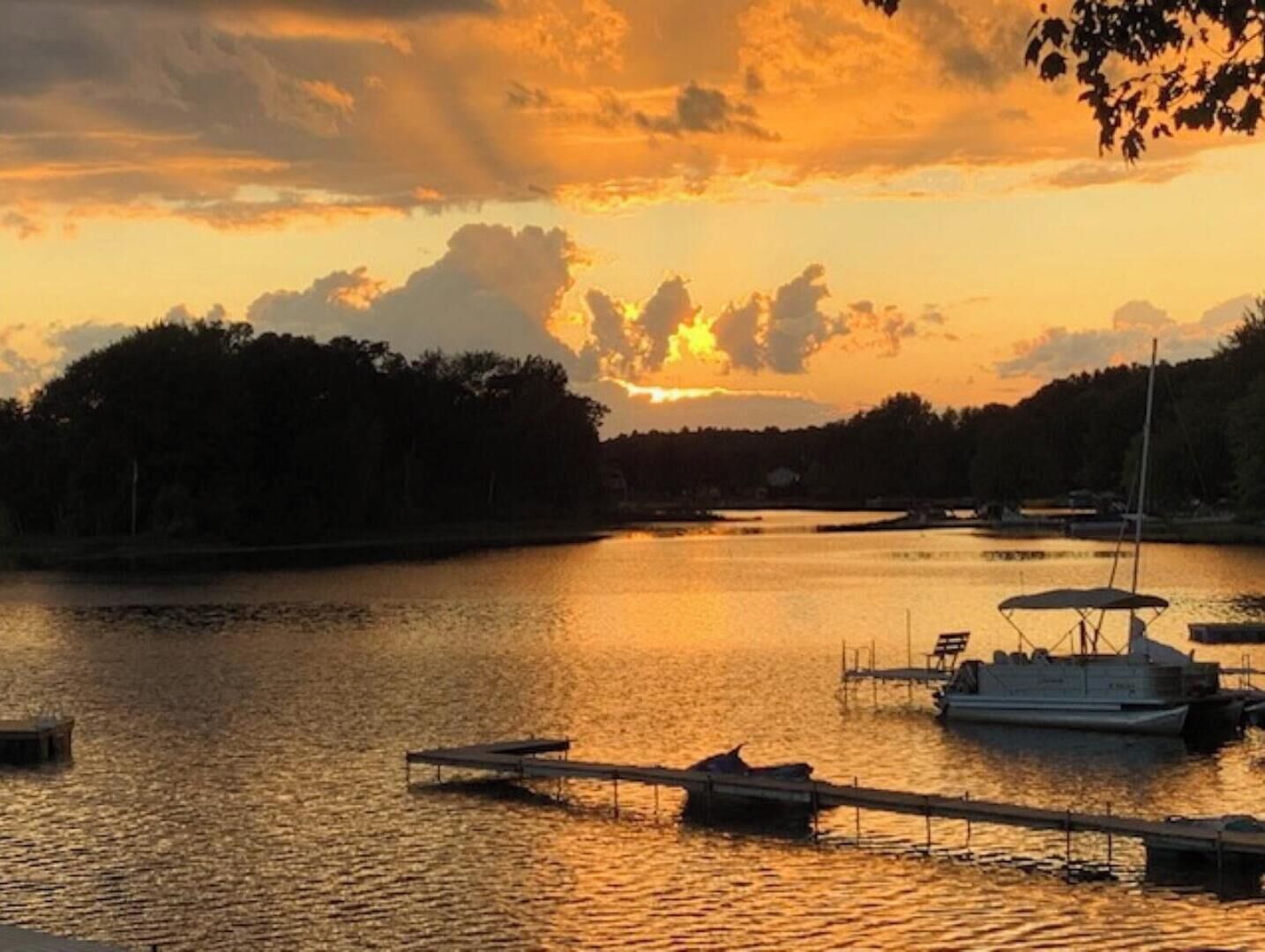 A sunset over a calm lake with boats docked at a pier.