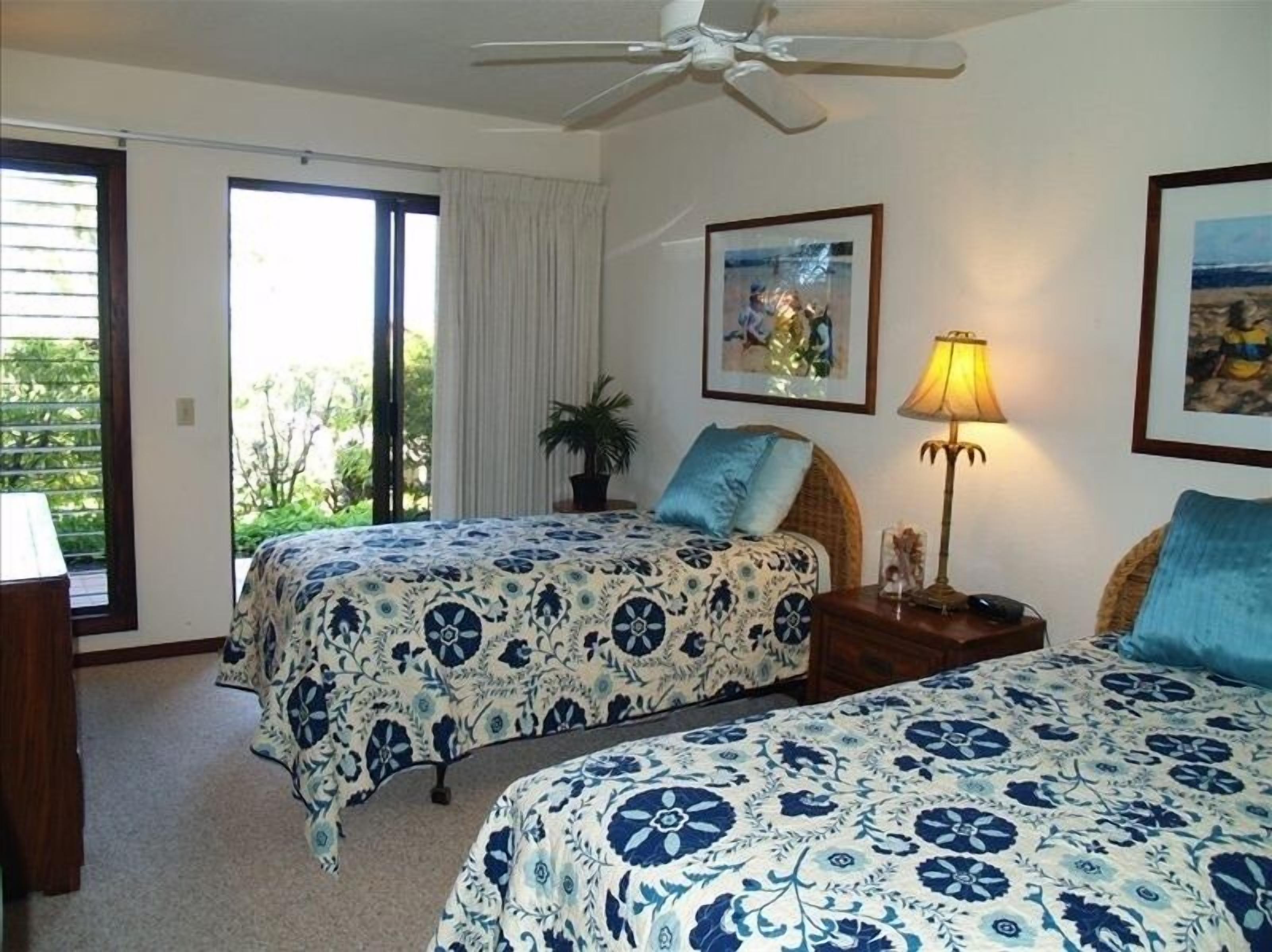 Ett hotellrum med två sängar, en takfläkt, ett fönster med gardiner, en lampa och inramade konstverk på väggarna.